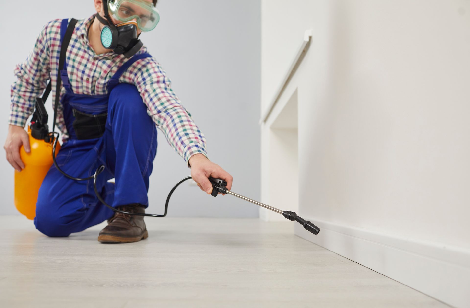 A pest control worker is spraying pesticide along the indoor baseboard. A pest control worker is spraying pesticide along the indoor baseboard.
