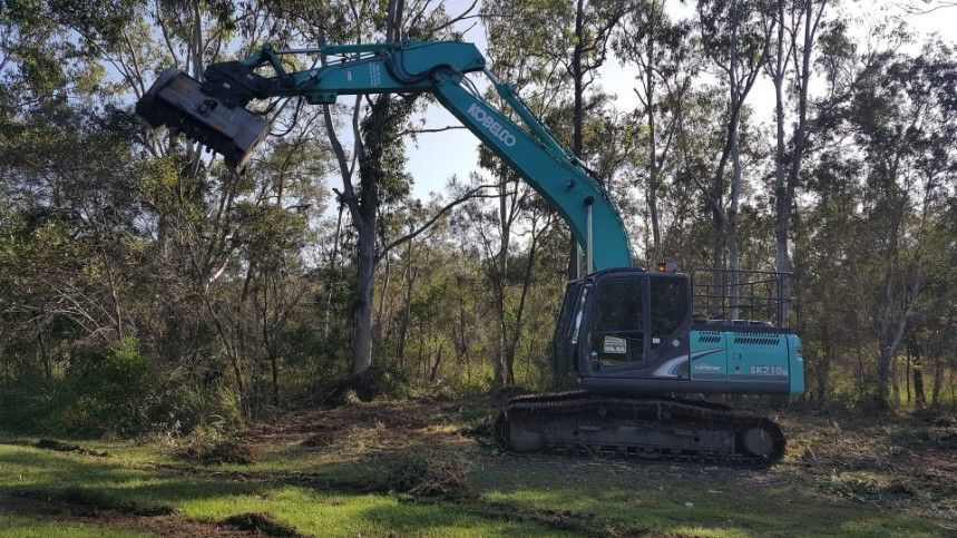 A Green Excavator in a Grassy Area Clearing Brush — Snell Earthworx In Craignish, QLD