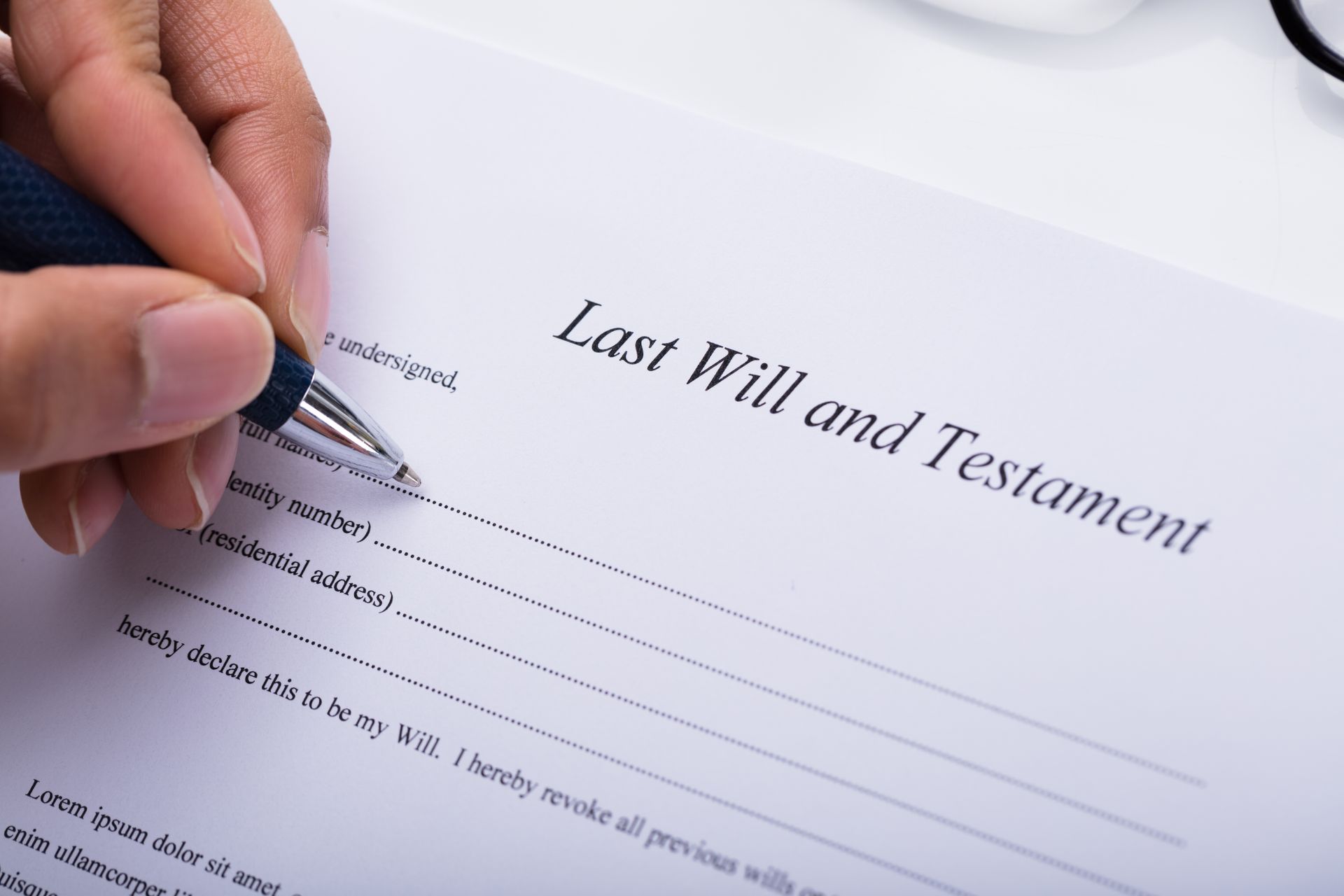 A person's hand uses a pen to fill out a legal document titled Last Will and Testament. A person's hand uses a pen to fill out a legal document titled Last Will and Testament.