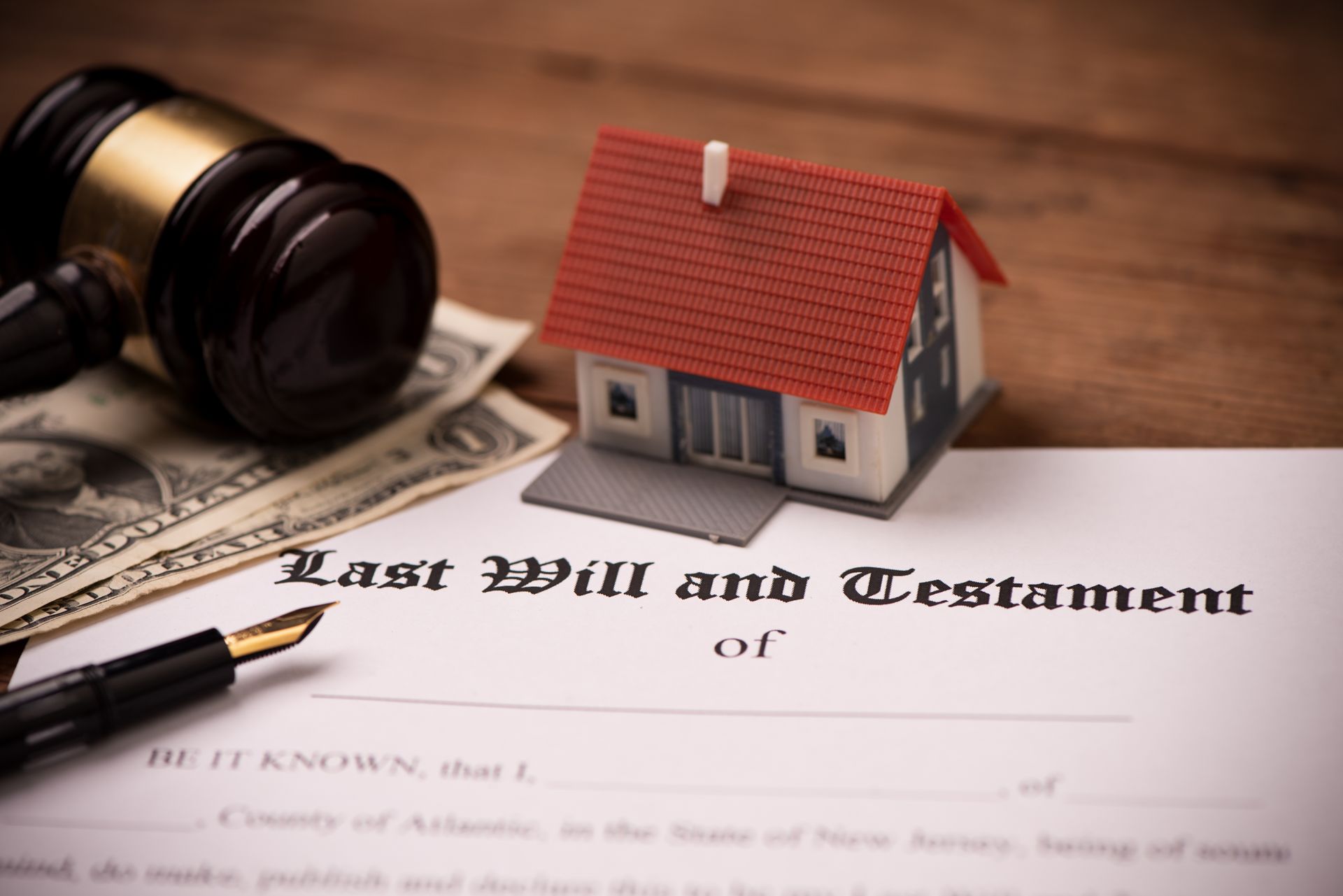 A document labeled Last Will and Testament sits on a wooden table with a toy house, a gavel, money, and a fountain pen. A document labeled Last Will and Testament sits on a wooden table with a toy house, a gavel, money, and a fountain pen.