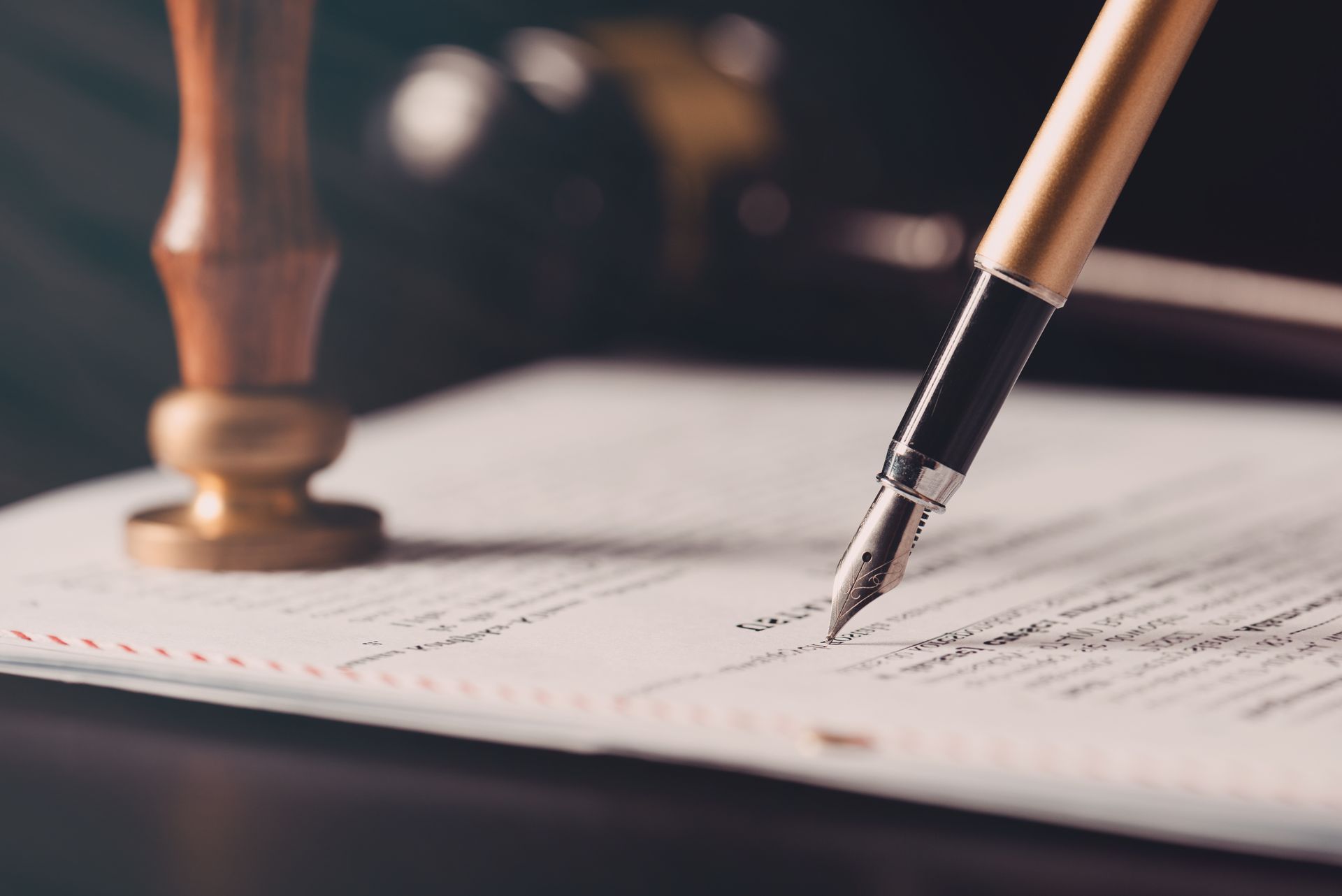 A fountain pen writes on a legal document beside a wooden wax seal stamper on a desk.