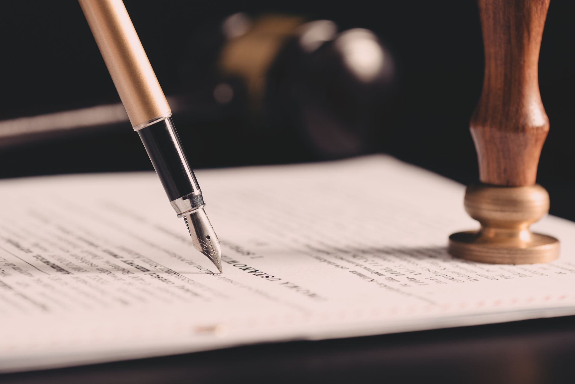 A fountain pen writes on a document next to a wooden notary seal against a dark background. A fountain pen writes on a document next to a wooden notary seal against a dark background.