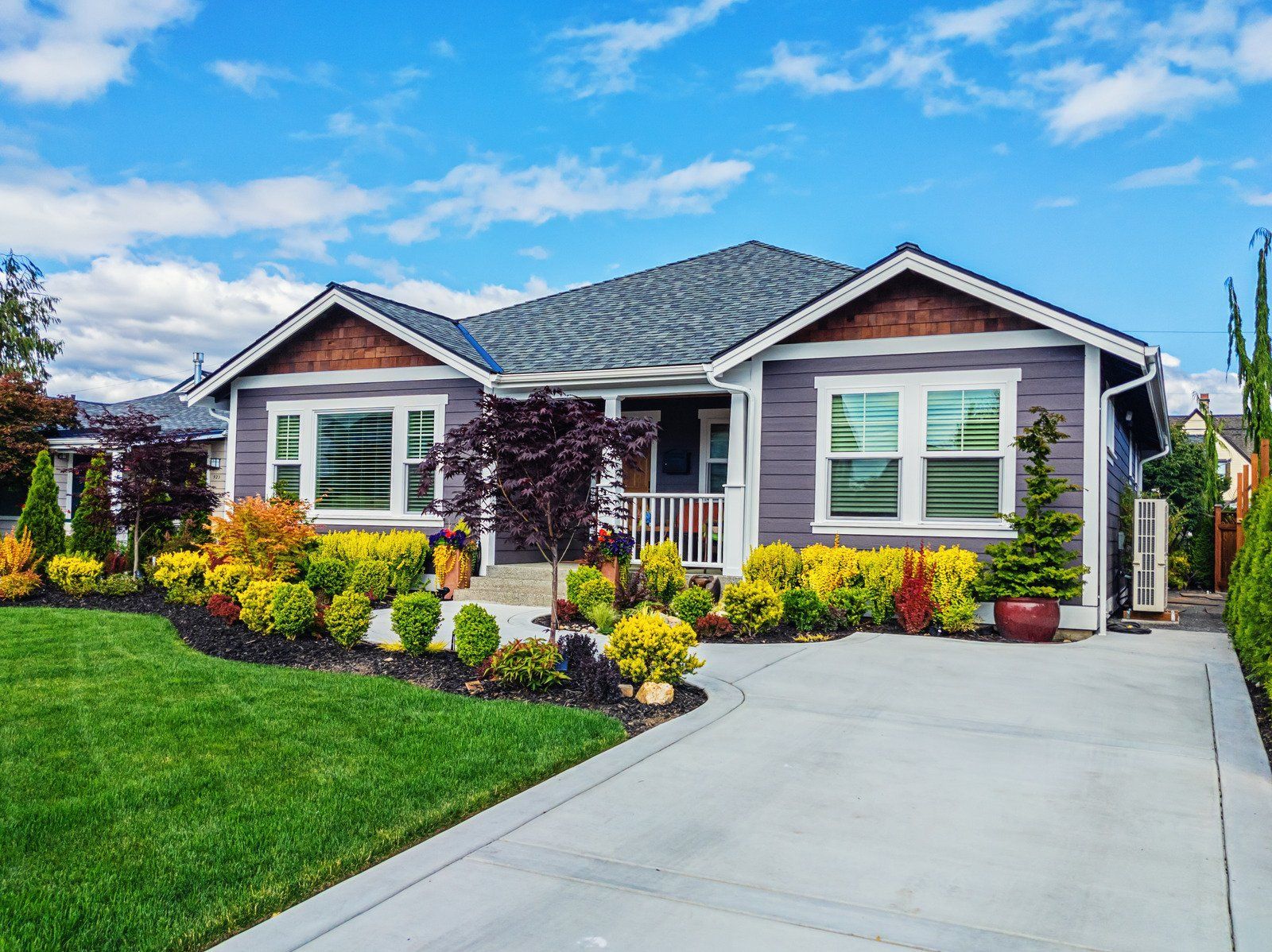 Purple house with landscaping, concrete driveway, and blue sky.