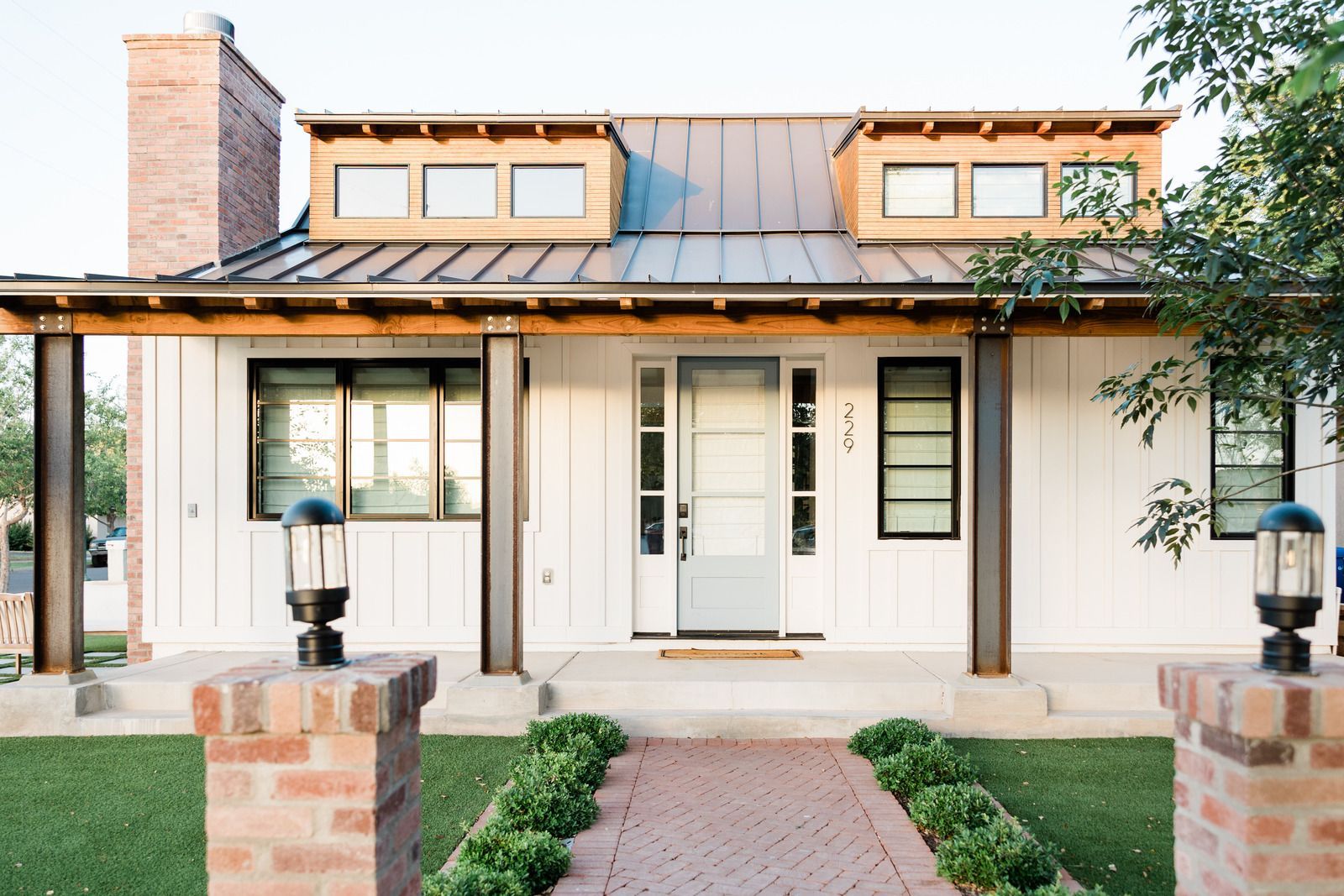 White house with a brick chimney and metal roof, porch, and a brick pathway.