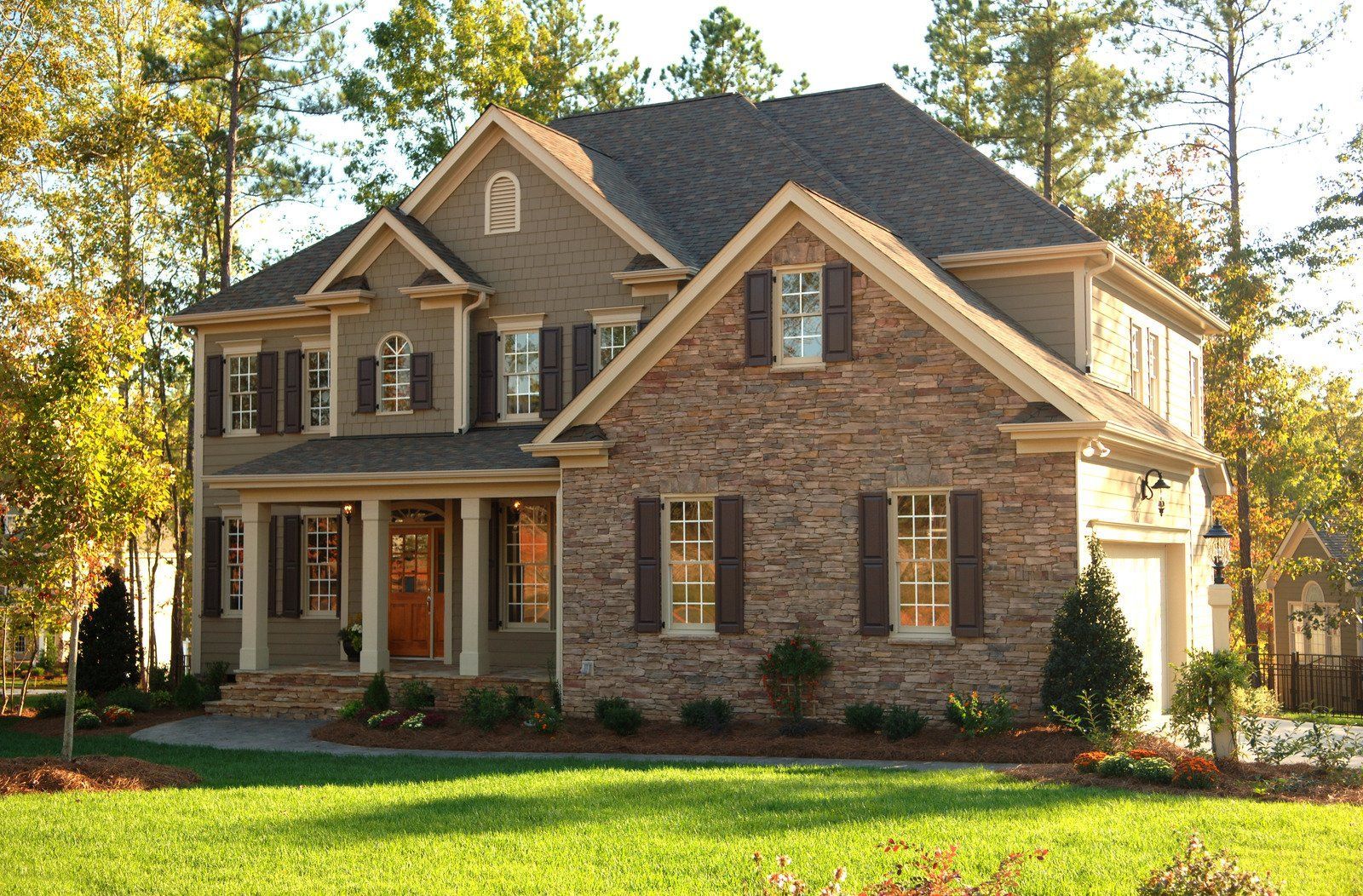 Two-story house with stone and siding exterior, brown shutters, green lawn, trees in background.