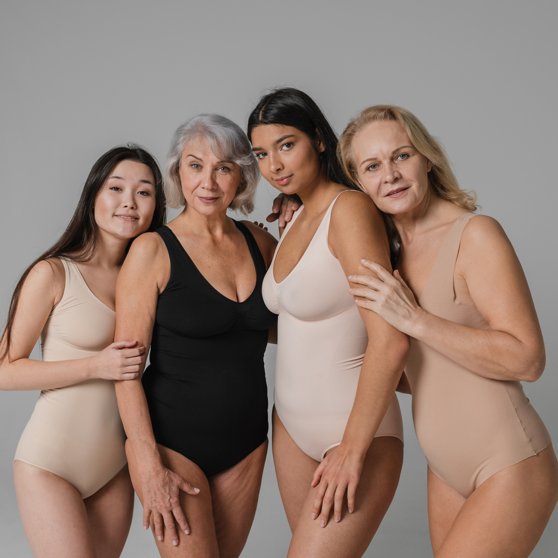 Quatre femmes en bodys aux tons neutres posent ensemble sur un fond gris uni.