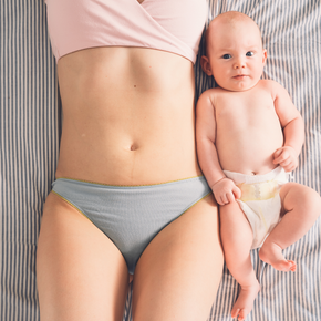 Personne en sous-vêtements gris tenant un bébé souriant sur fond rayé
