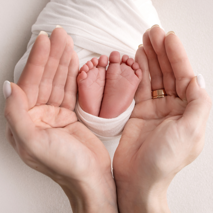 Les pieds d'un nouveau-né, bercés par deux mains d'adulte, sont enveloppés dans un doux tissu blanc.