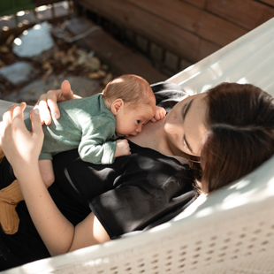 Un parent berce son bébé endormi dans un hamac ensoleillé à l'extérieur.