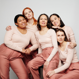 Cinq femmes vêtues de tenues rose pâle assorties posent ensemble sur un fond gris clair.