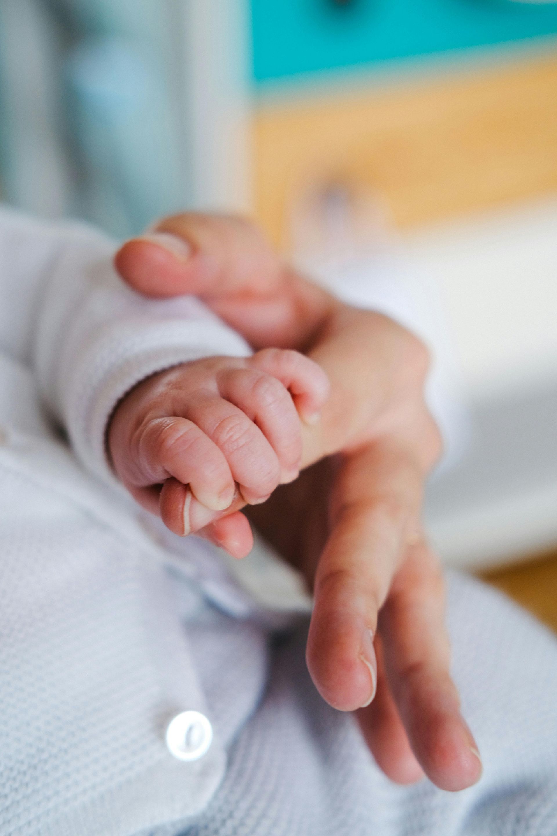 Gros plan sur la main d'un bébé tenant un doigt d'adulte, sur un t-shirt blanc flou.