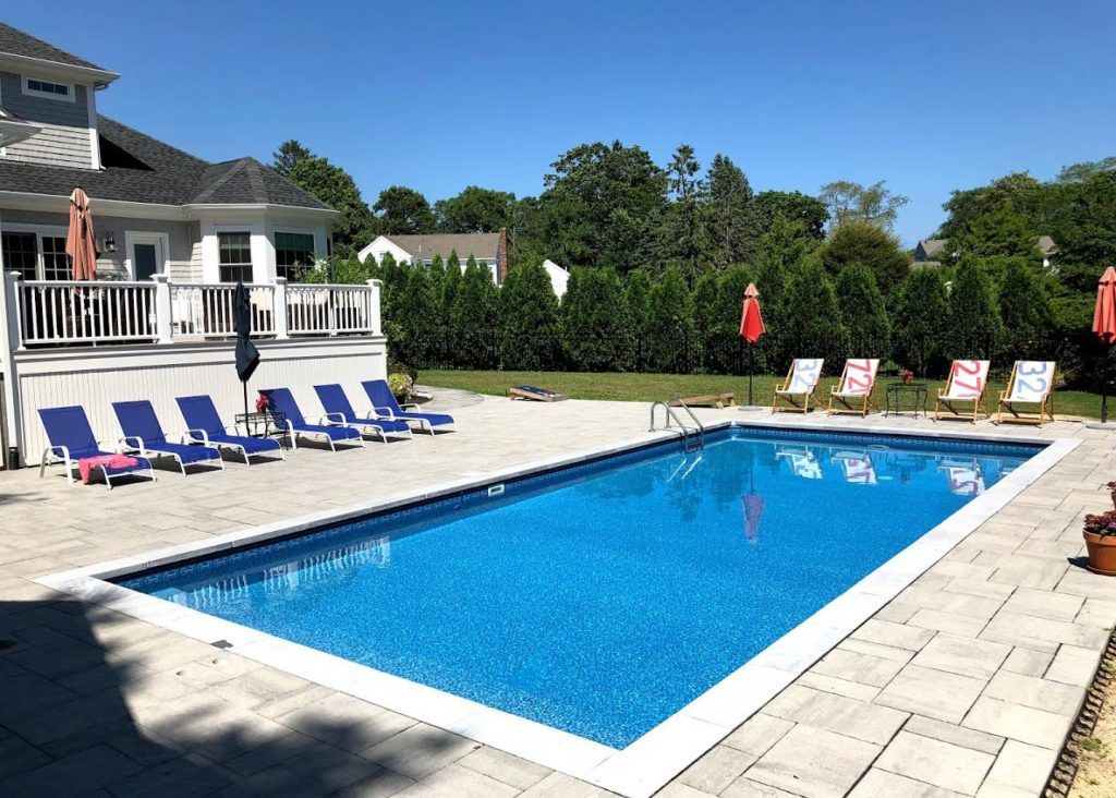 A large swimming pool is surrounded by chairs and umbrellas in front of a house.
