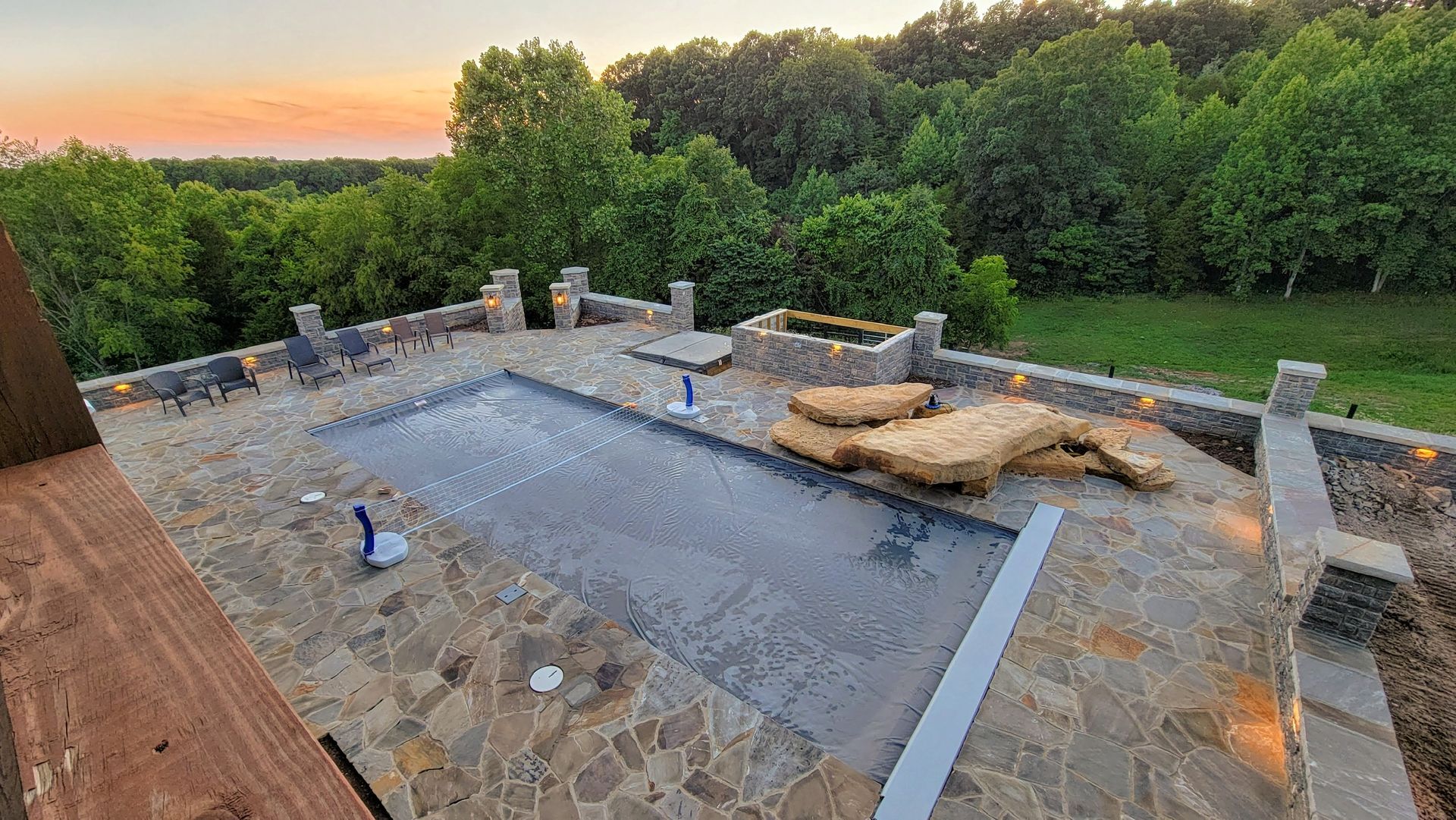 Stone patio under construction at sunset, with tools and materials beside a wooded hillside.