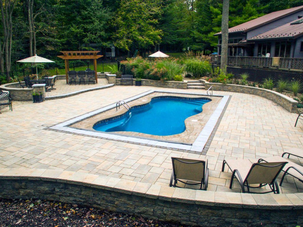 A large swimming pool is surrounded by a patio with chairs and umbrellas.