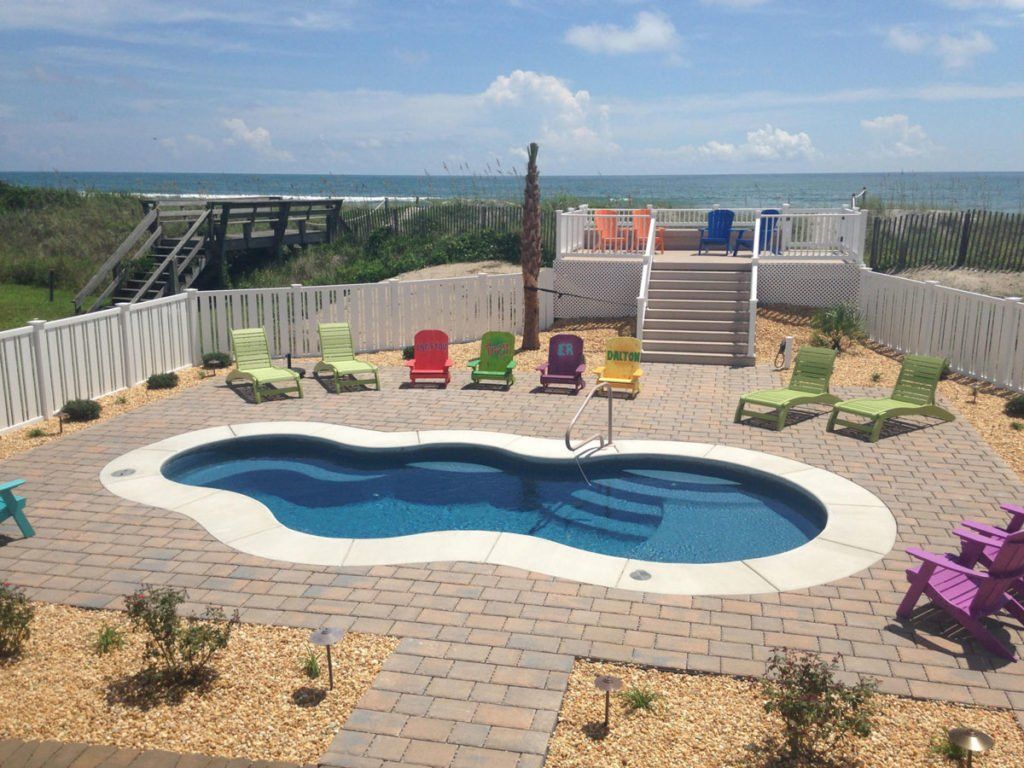 A large swimming pool surrounded by chairs and a deck overlooking the ocean.