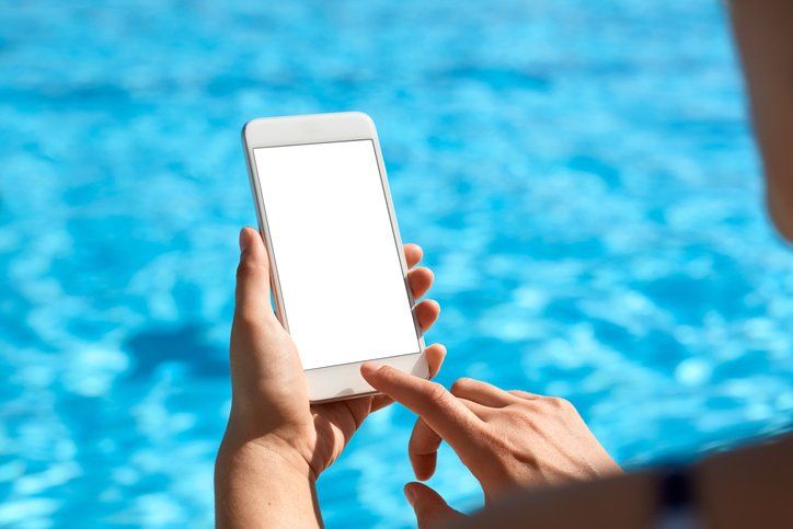 A person is holding a cell phone in front of a swimming pool.
