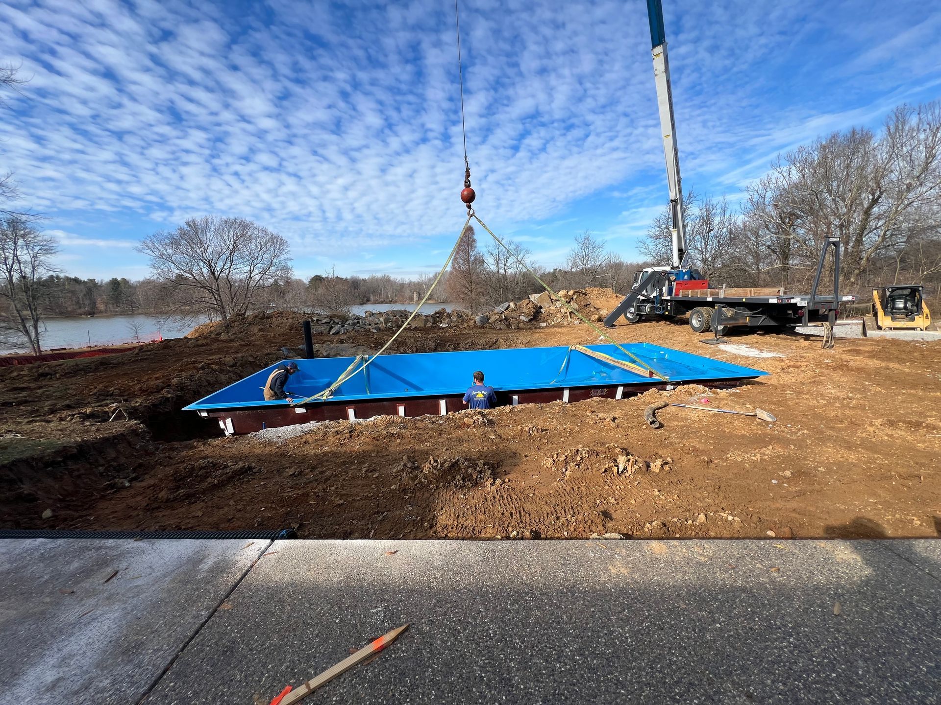 A crane is lifting a blue swimming pool into the ground.