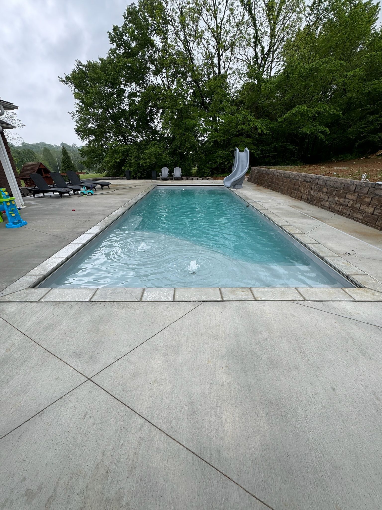 Rectangular outdoor pool with turquoise water, concrete deck, and trees in the background