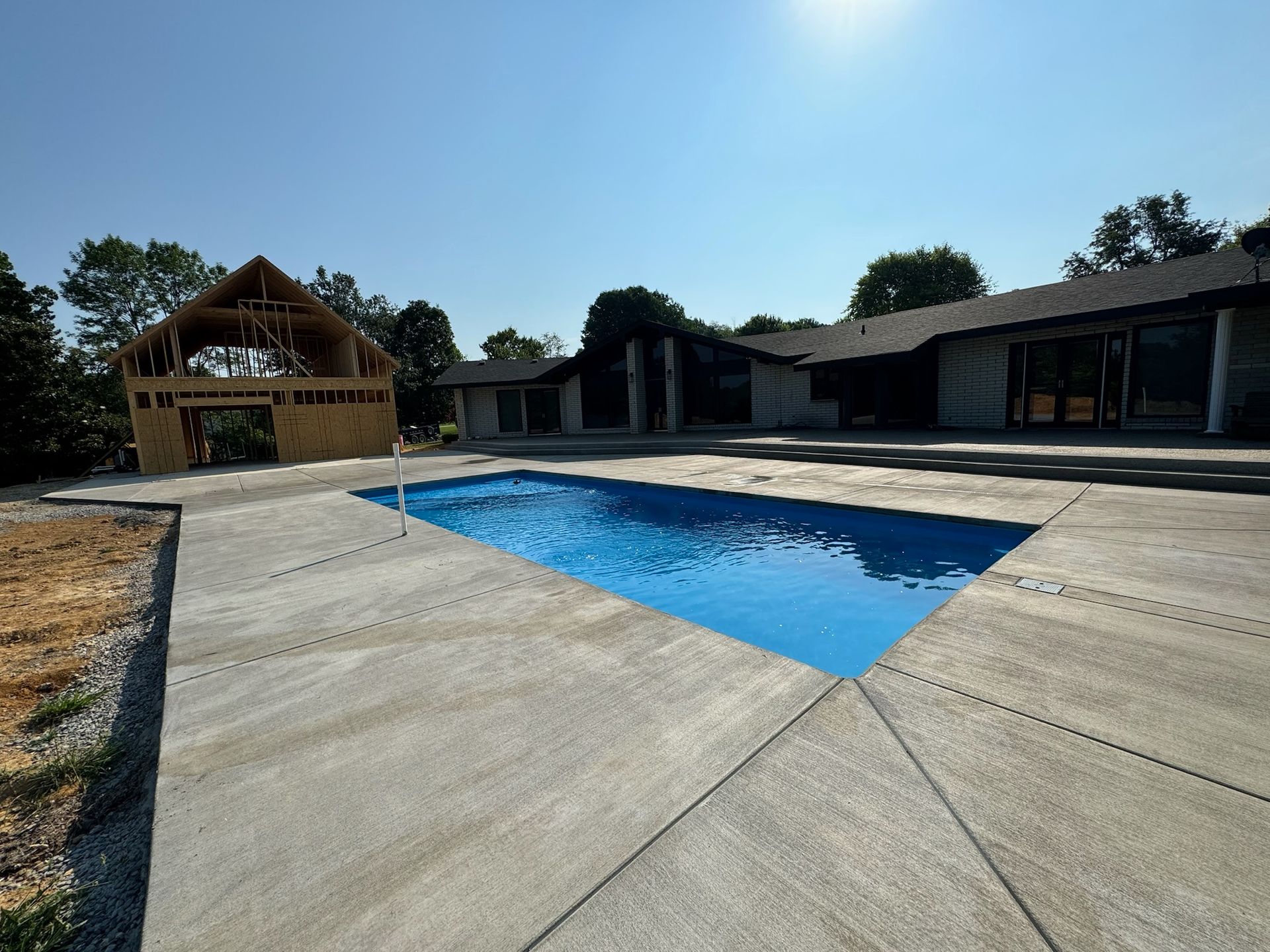 Backyard pool with a concrete deck and a house under a sunny blue sky