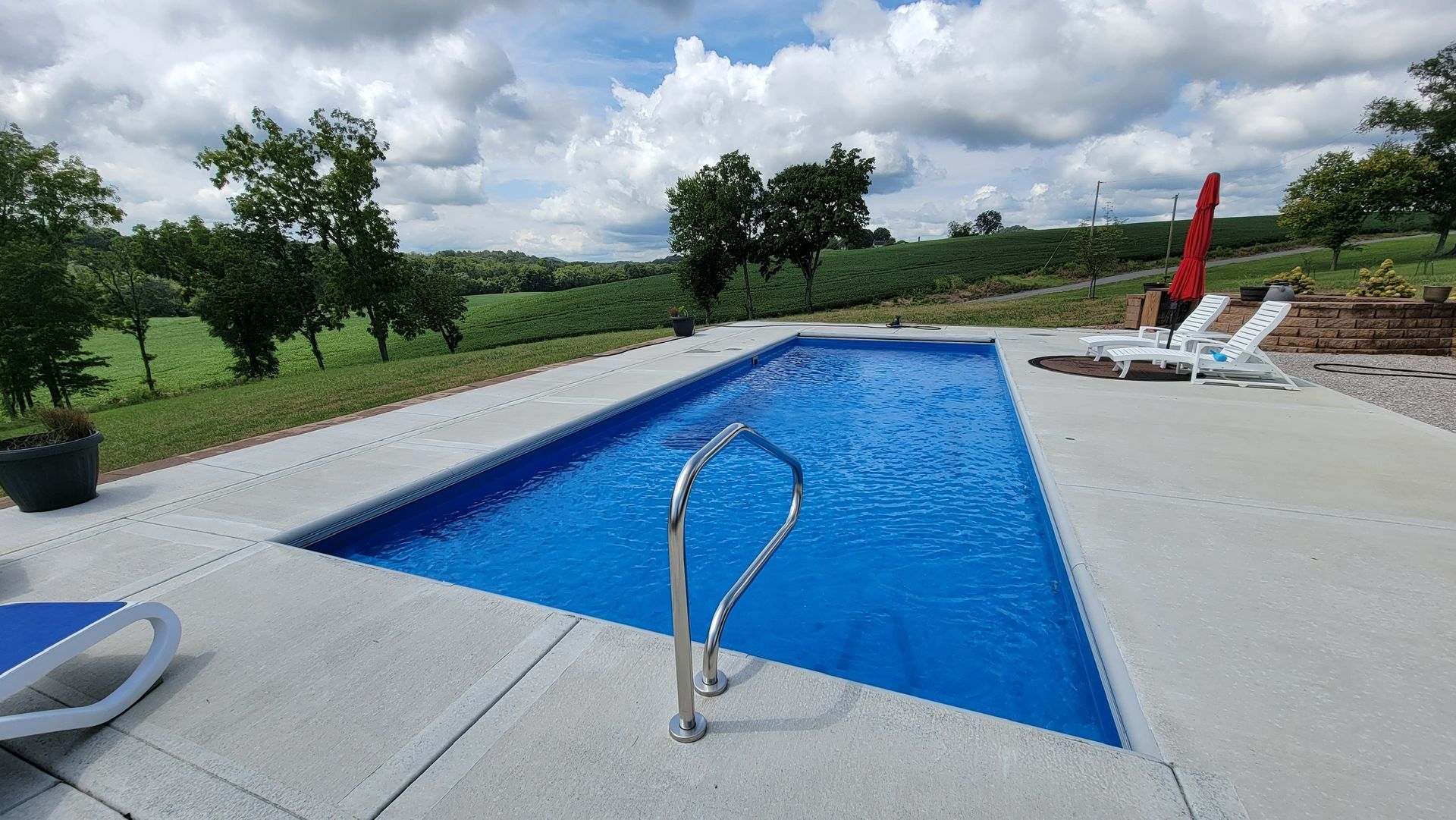 Outdoor swimming pool with blue water, white deck, and lounge chairs overlooking a green landscape
