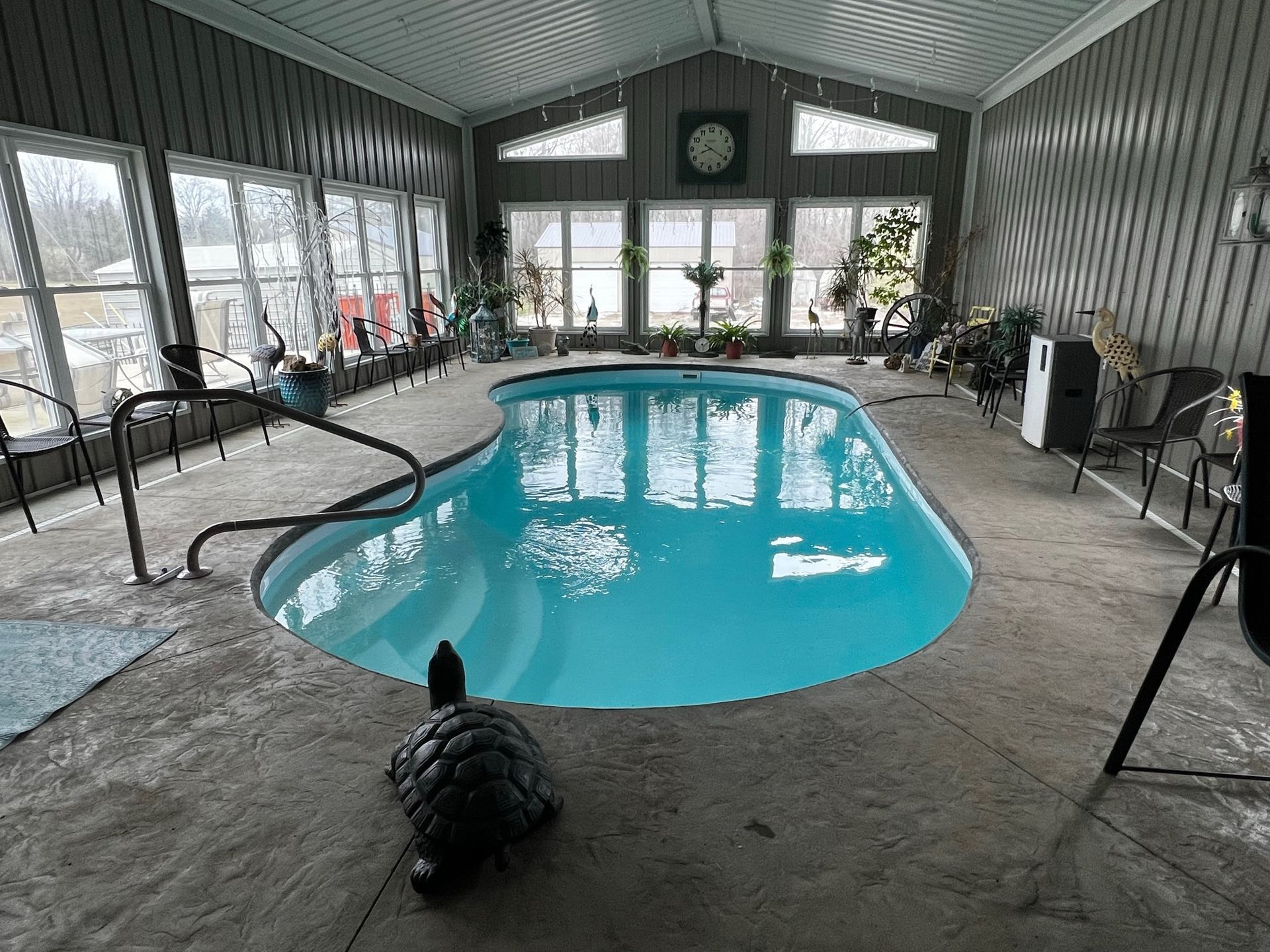 Indoor pool with bright blue water, surrounded by lounge chairs in a covered sunroom.