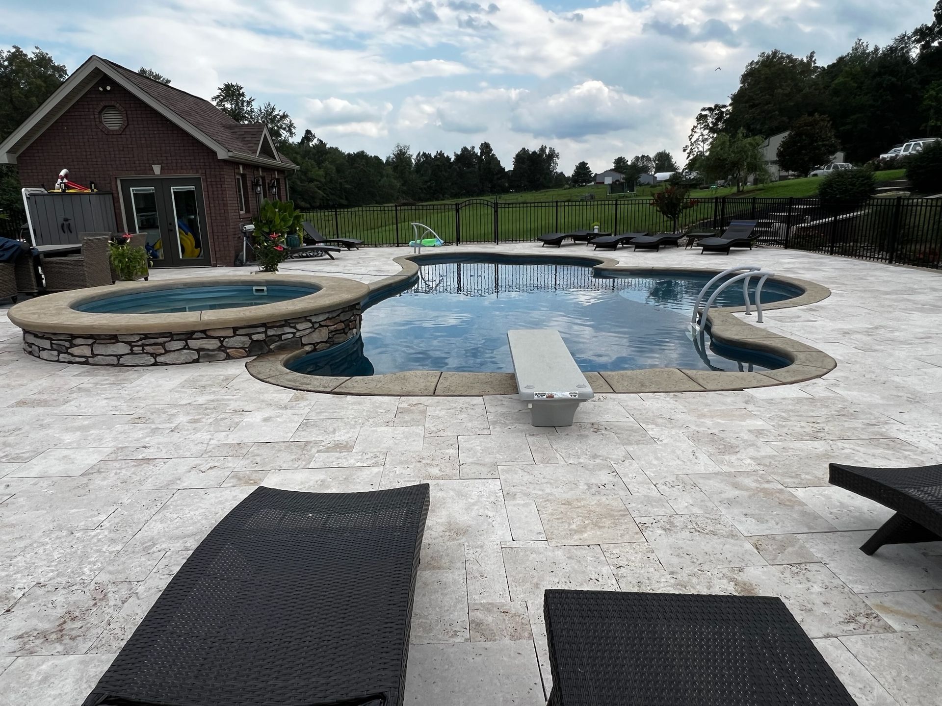 Backyard pool with stone patio, hot tub, and lounge chairs beside a brick house