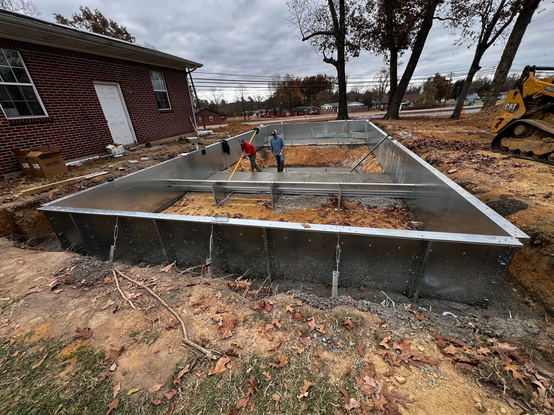 A large metal foundation is being built in front of a brick house.