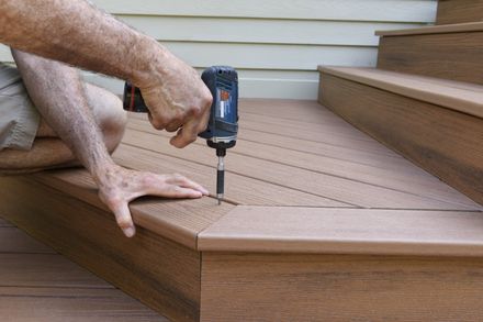 A man is using a drill on a wooden deck.
