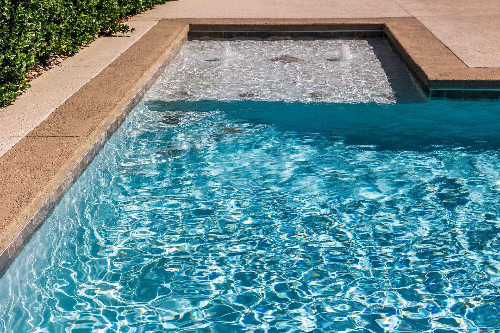 Blue swimming pool with rippling water and a tan stone edge beside a patio