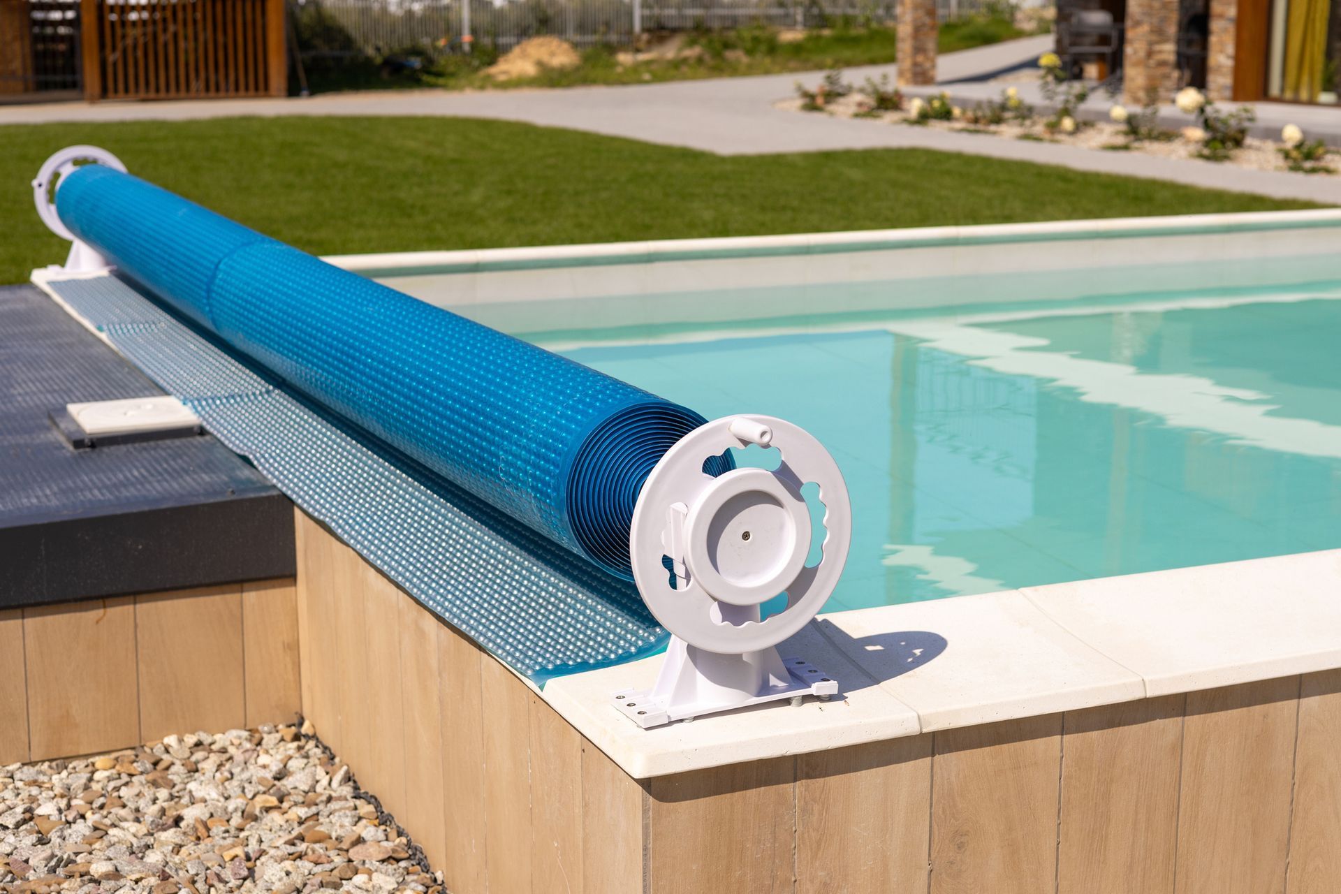 Blue pool cover roller on the edge of a backyard swimming pool