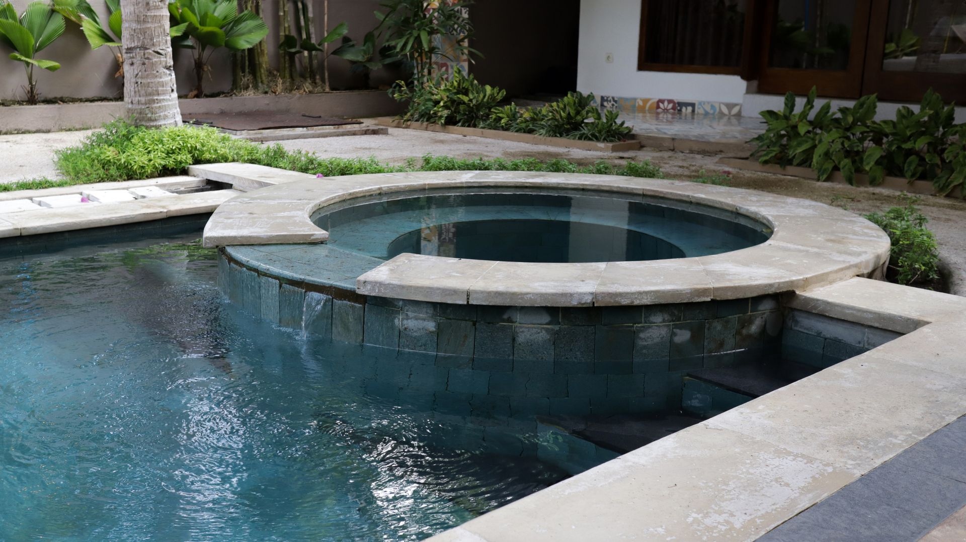 Stone-lined pool with a raised circular spa in a tropical courtyard