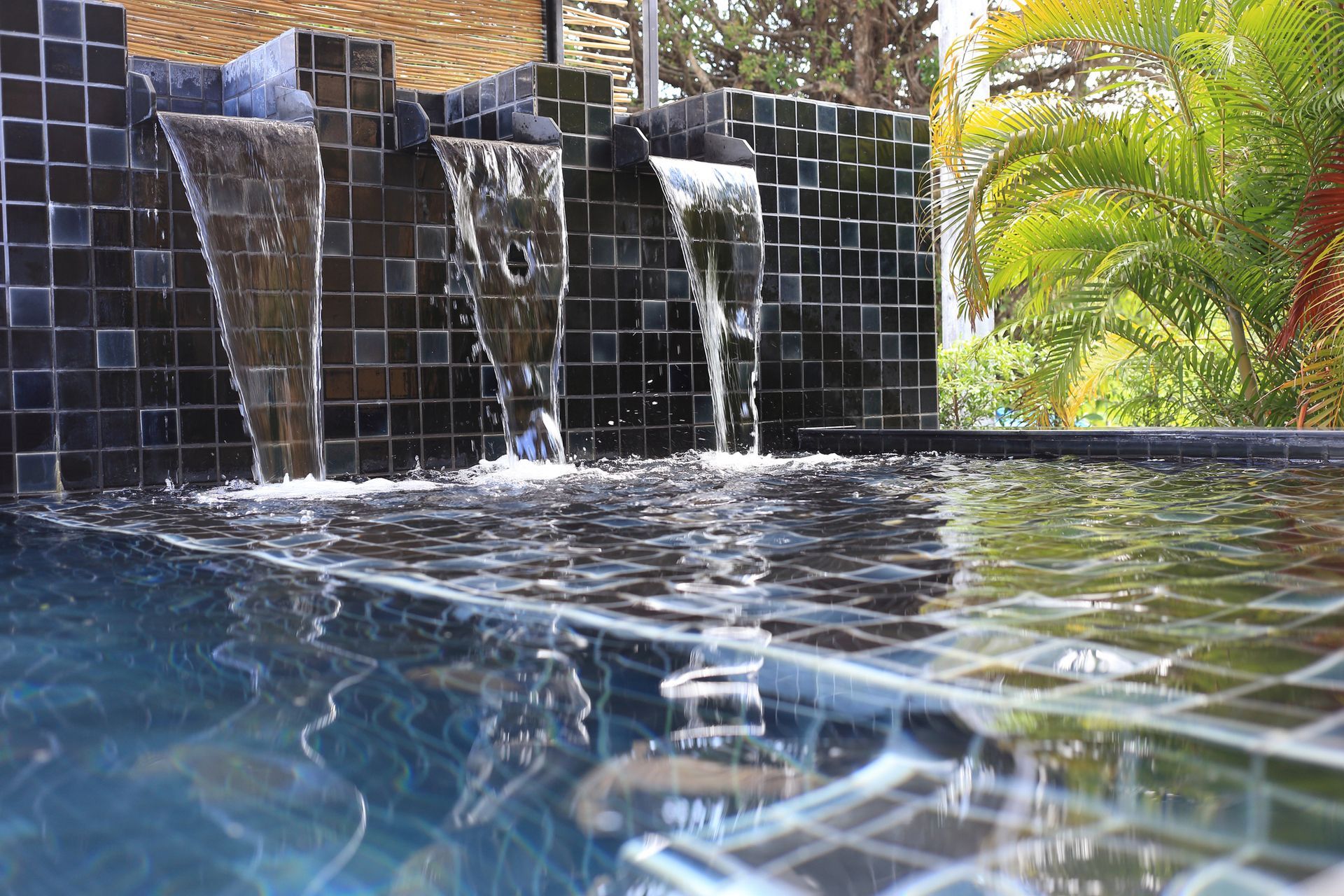 Tiled waterfall fountain spilling into a calm blue pool with palm trees in the background