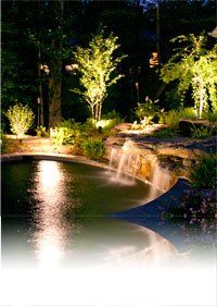 A pond with a waterfall in the middle of it is lit up at night.
