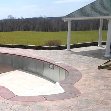Empty outdoor pool with curved stone deck and white gazebo overlooking a grassy field.