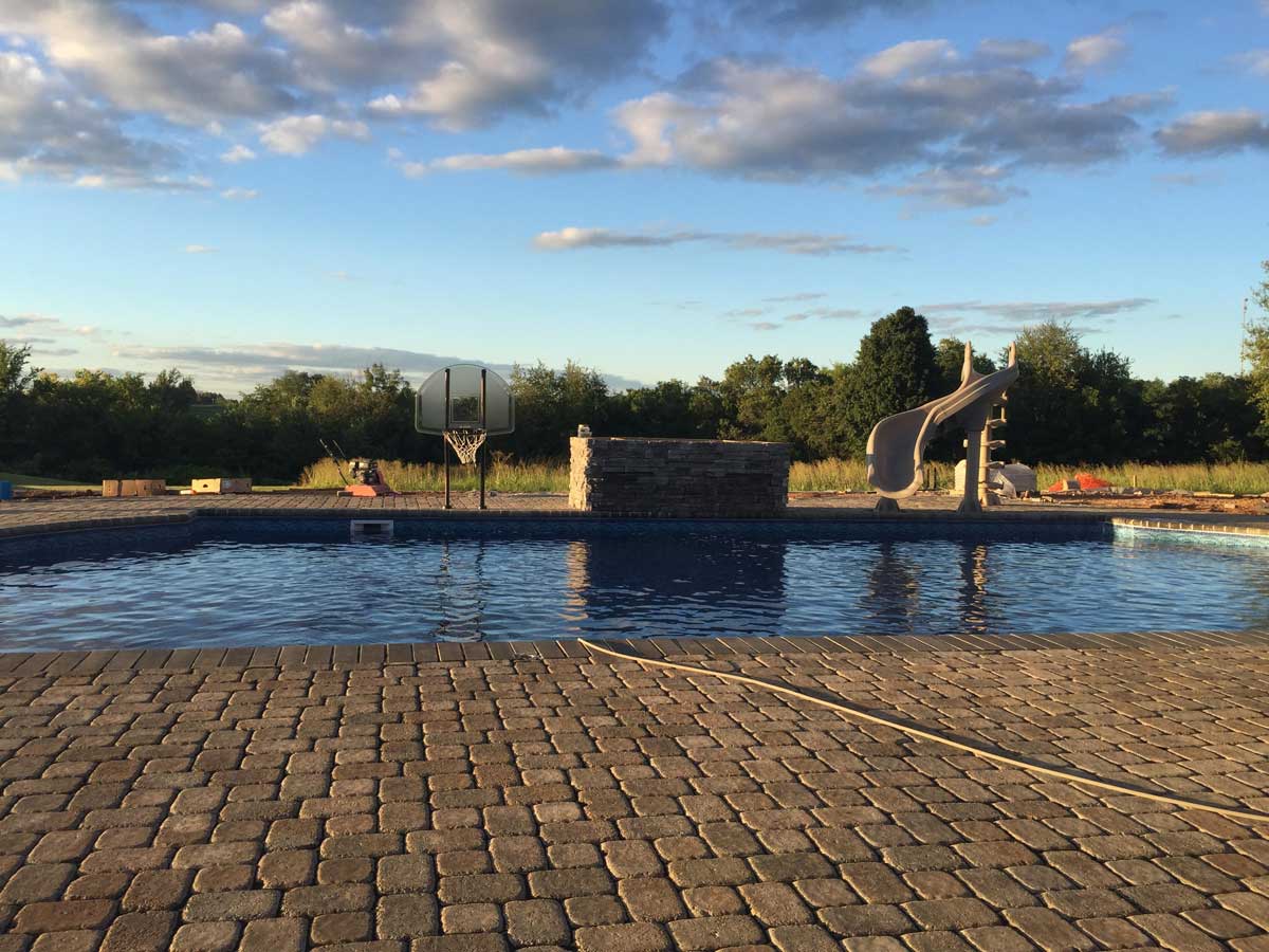 A swimming pool with a slide and a basketball hoop in the background.
