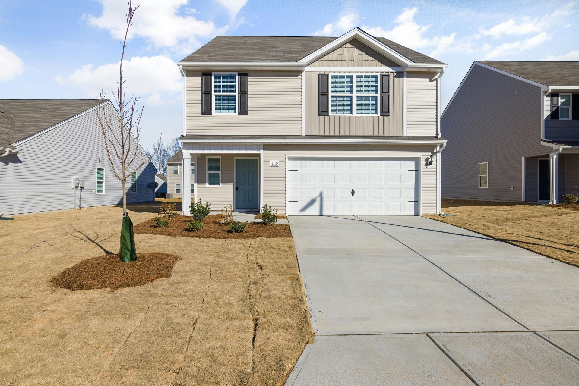 Two-story house with beige siding, white garage door, and concrete driveway on a sunny day.