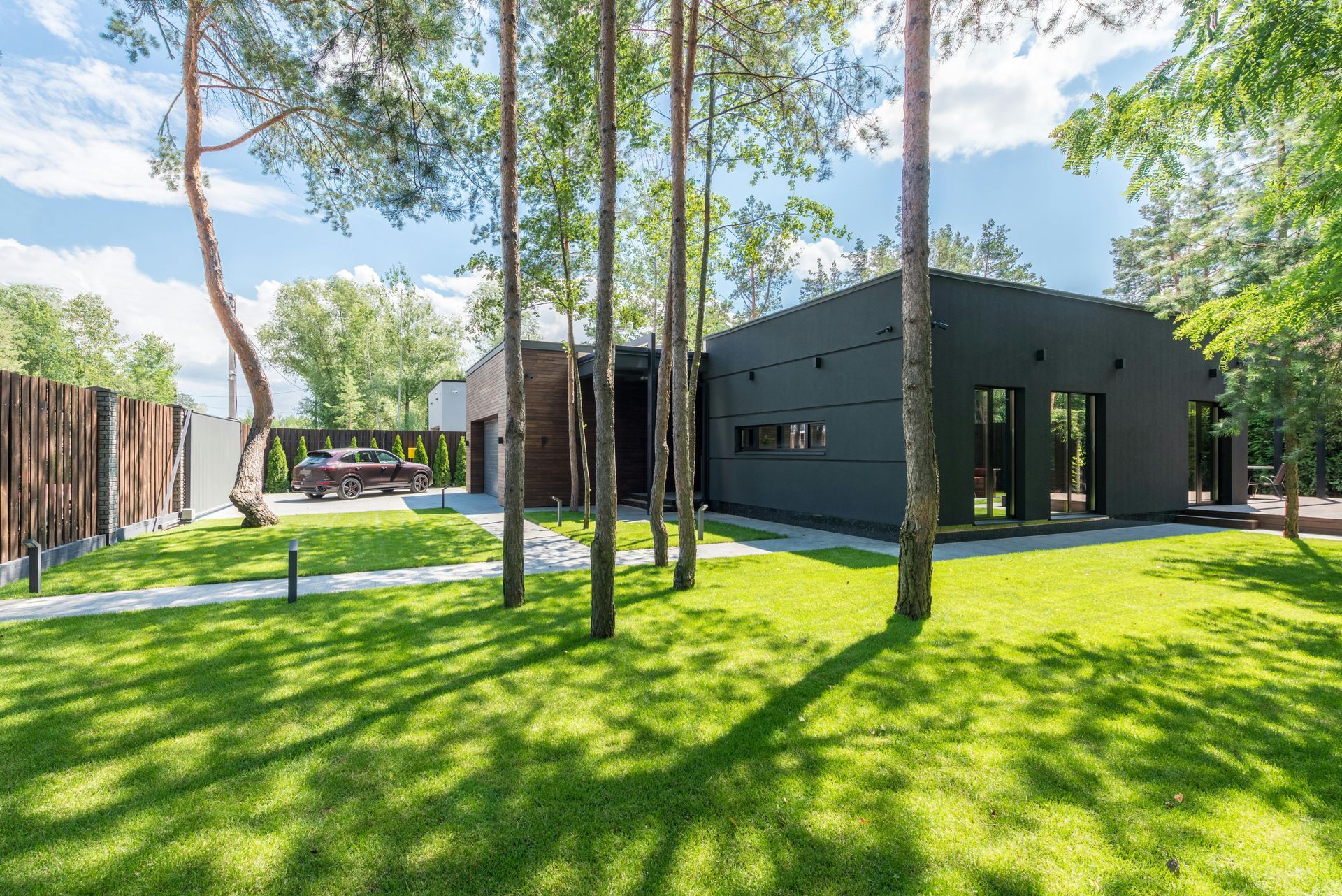 Modern black house with large windows, green lawn, and trees.