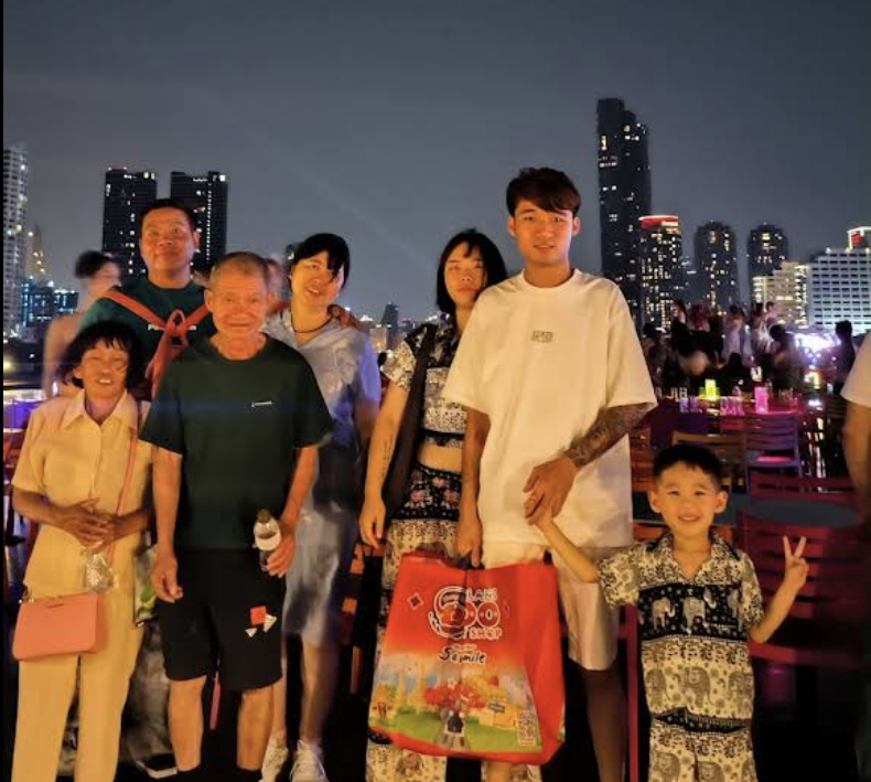 一群人在夜色中於海濱長廊合影，背景是城市天際線的燈光。