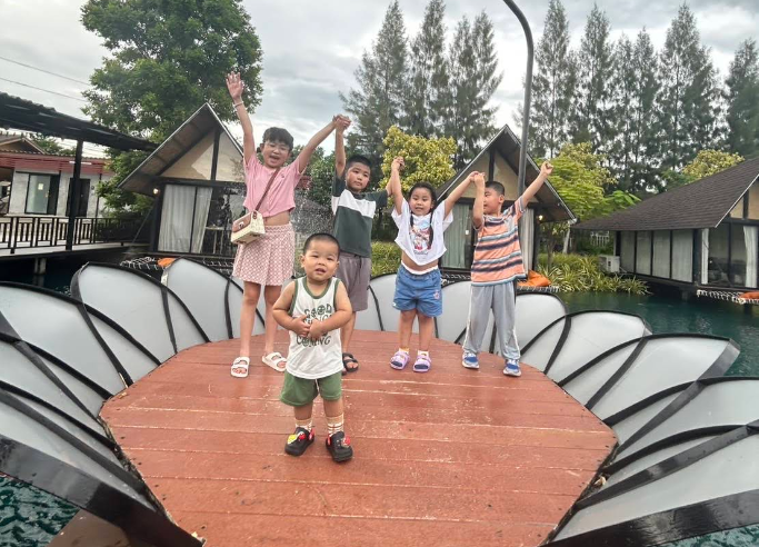 五個孩子在戶外公園的木橋上舉起雙臂擺姿勢拍照。