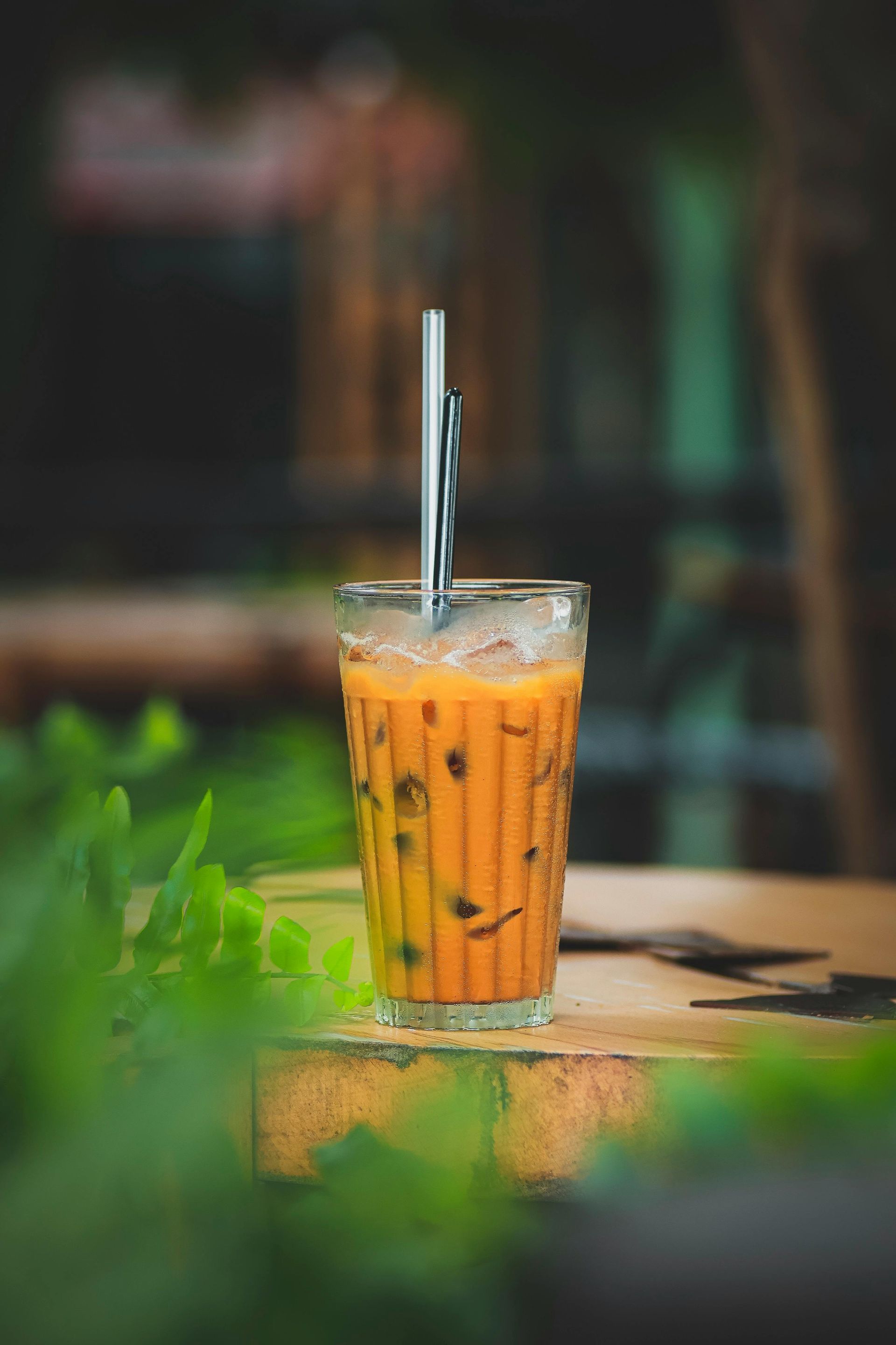 桌上放著一杯高高的冰橙茶，插著吸管，咖啡館背景模糊。