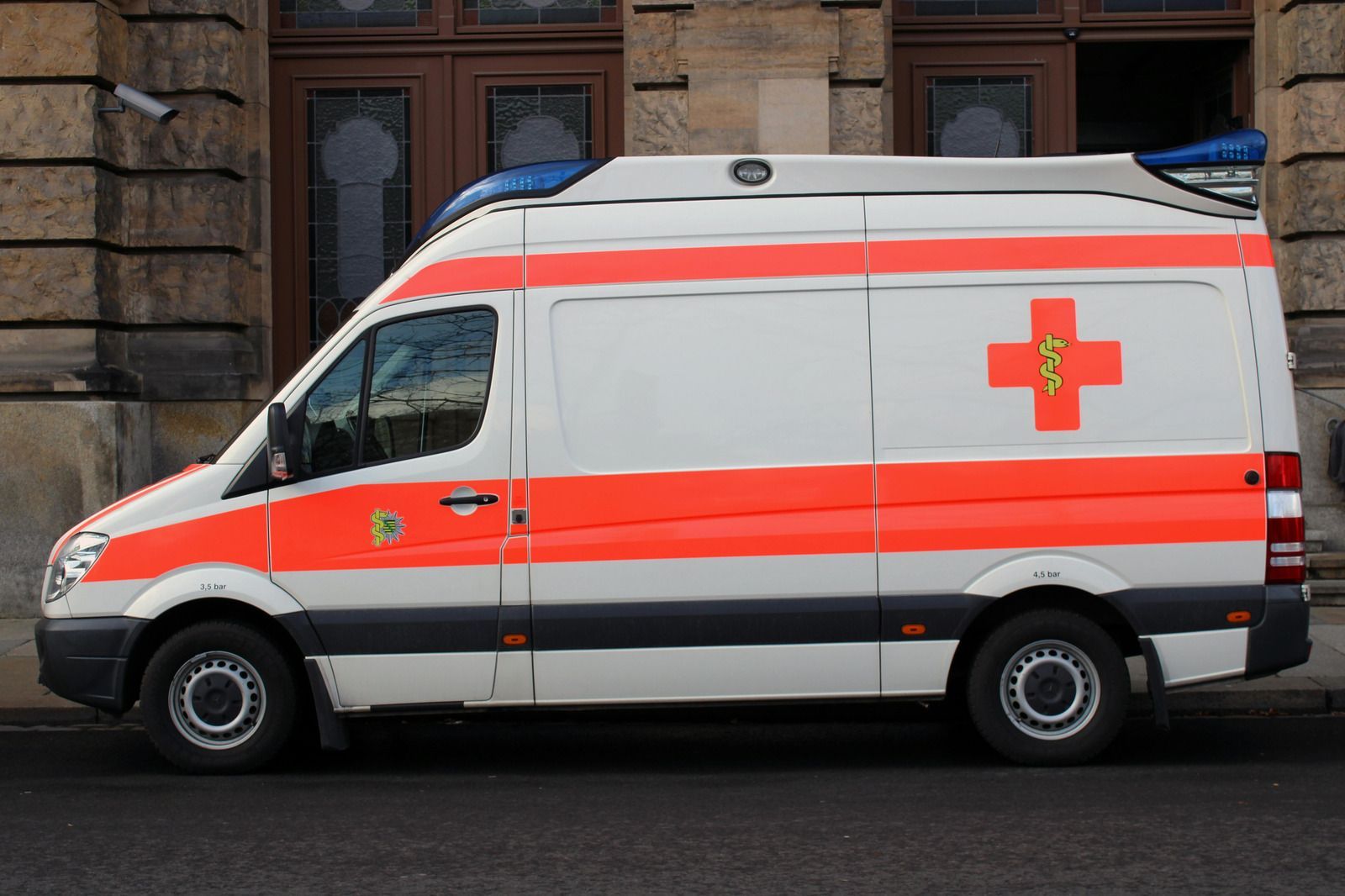 White and red ambulance parked on a street; red cross on the side.