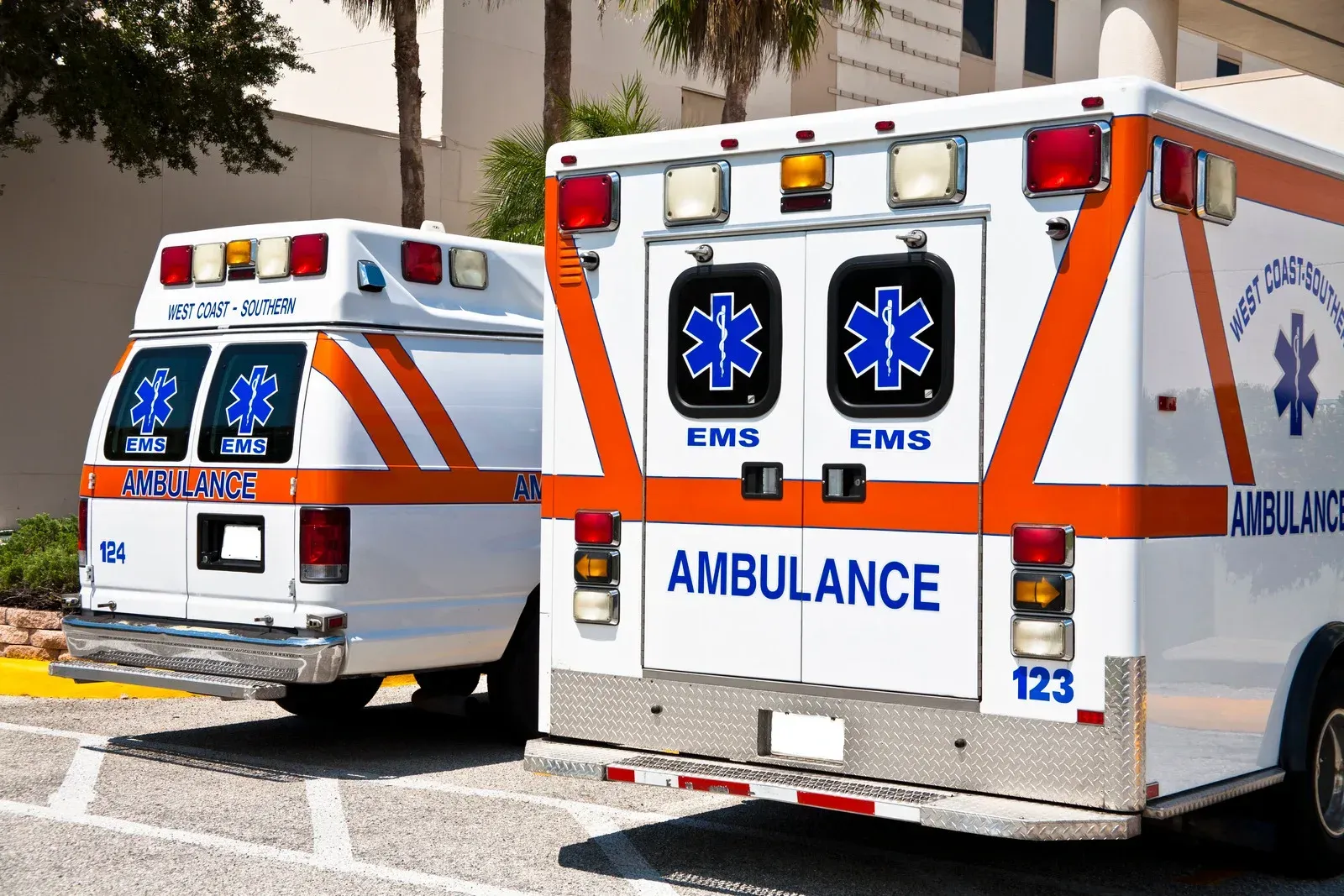 Two white and orange ambulances parked in front of a building with palm trees.