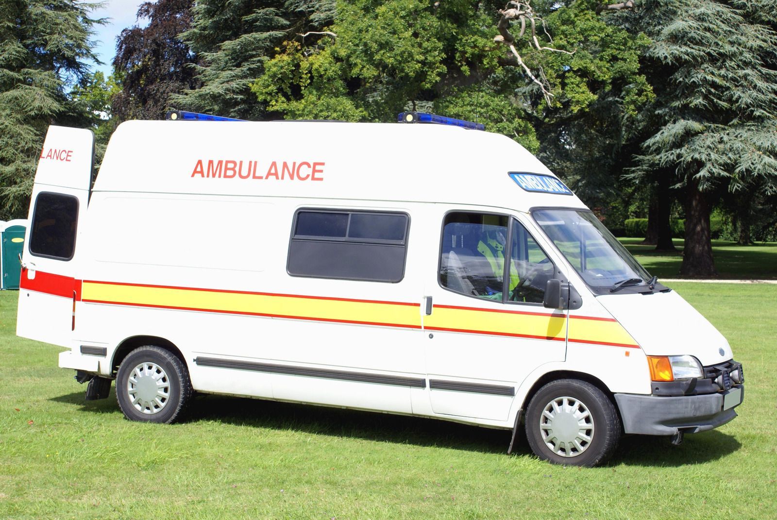 White ambulance van parked on grass. Has red and yellow stripes, 