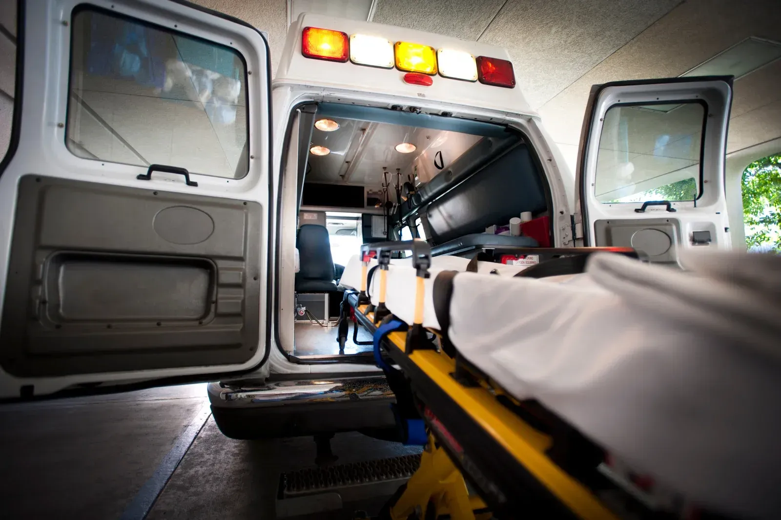 Ambulance interior with stretcher extended, doors open, emergency lights on.