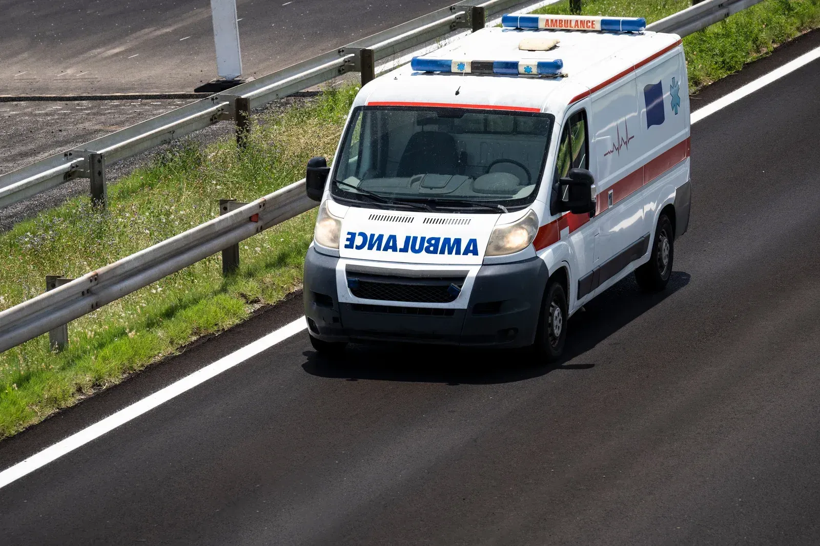 Ambulance driving on a highway, with flashing lights. White van with red stripes.