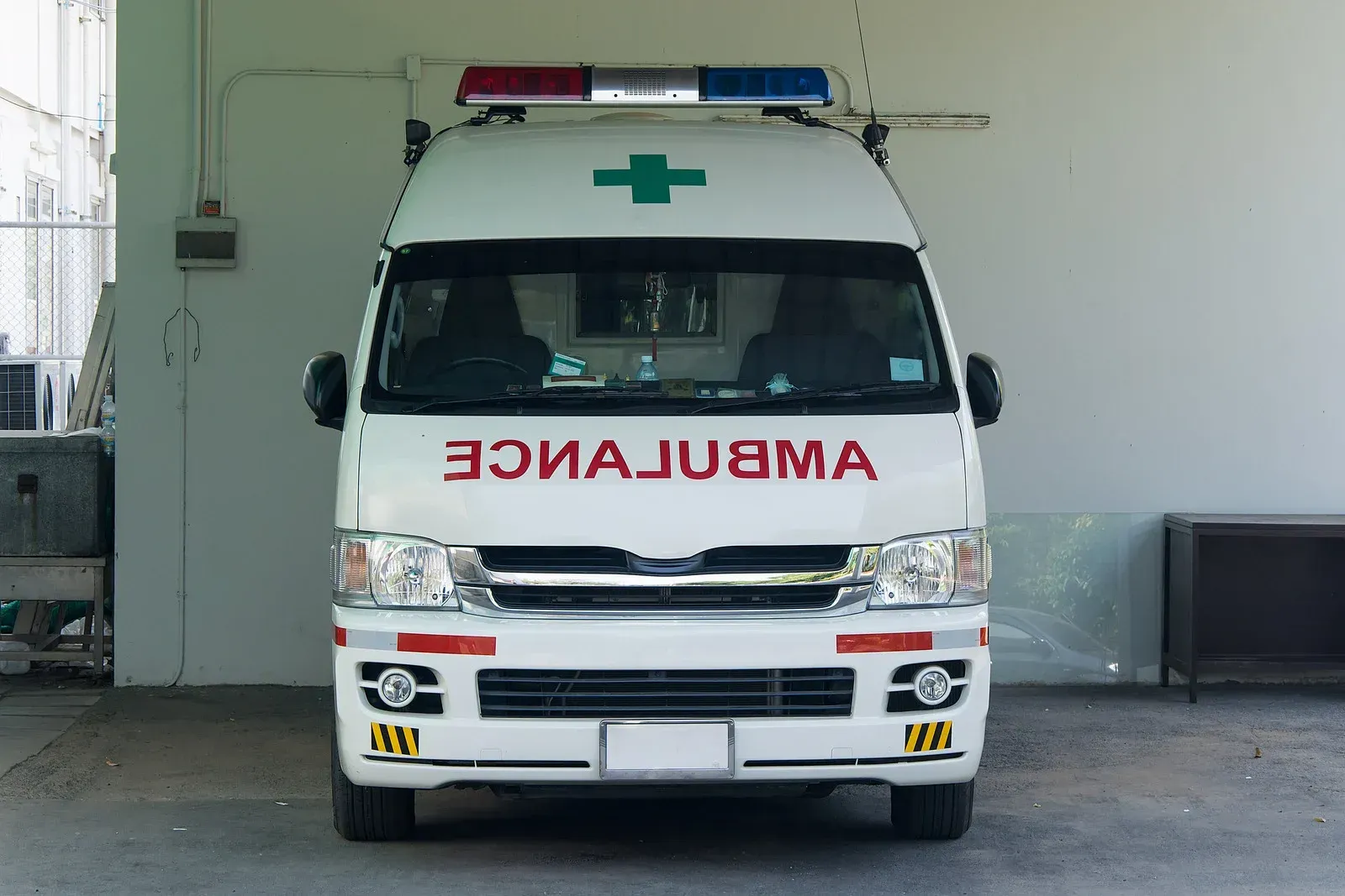 White ambulance with red and blue lights, a green cross, and 
