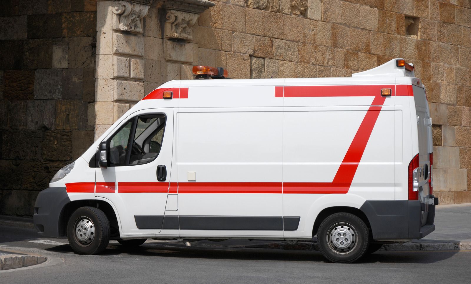 White ambulance with red stripes parked in front of a stone building.