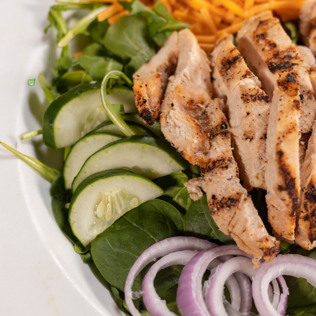 A white plate topped with grilled chicken , cucumbers , onions and spinach.
