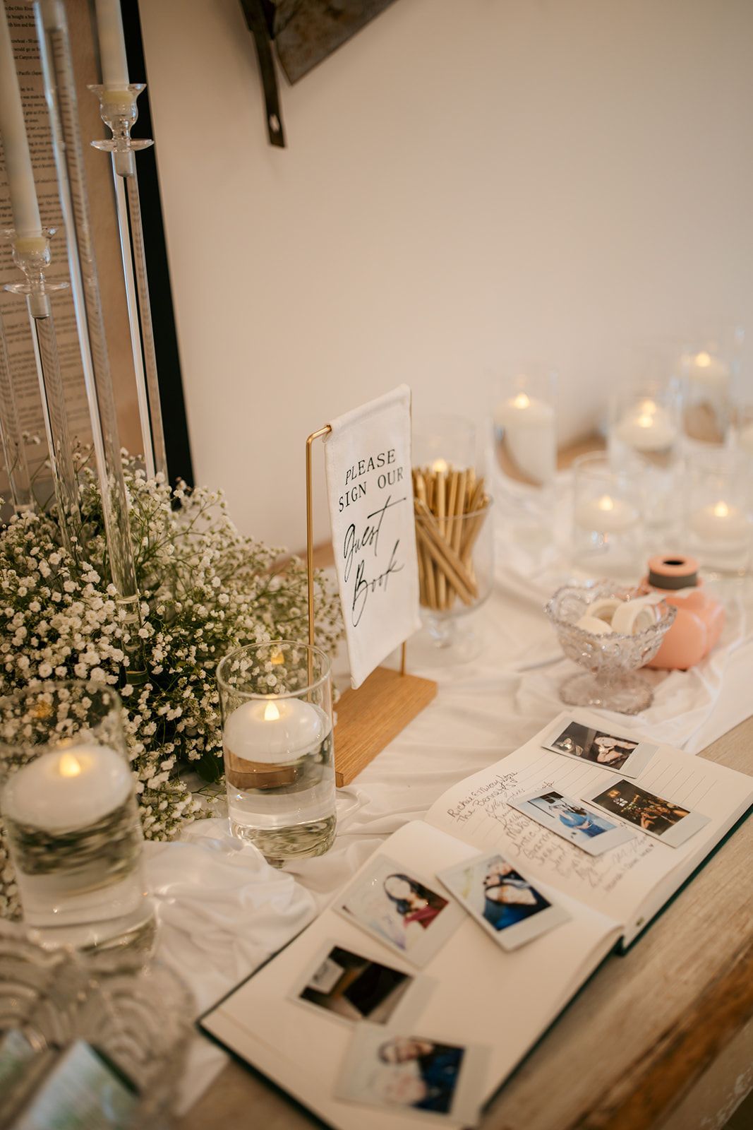 Decorated table with candles, flowers, glasses, and an open book in a soft-lit indoor setting