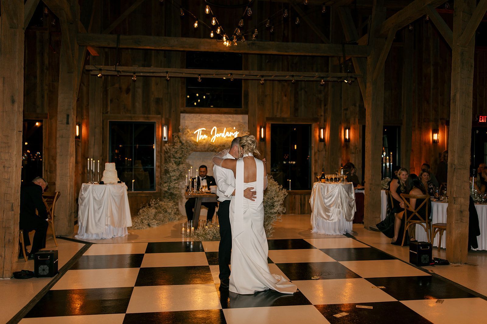 Bride and groom dancing in a rustic banquet hall with black-and-white checkered floor